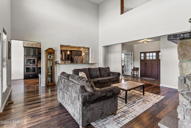 living area with dark wood-style floors, baseboards, a high ceiling, and visible vents