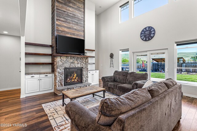 living area featuring a towering ceiling, dark wood-style floors, baseboards, and a stone fireplace