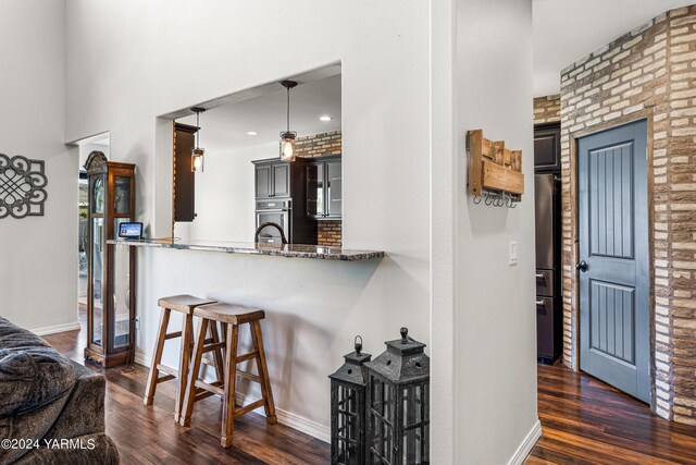 kitchen featuring dark stone counters, dark wood-style floors, glass insert cabinets, decorative light fixtures, and a peninsula