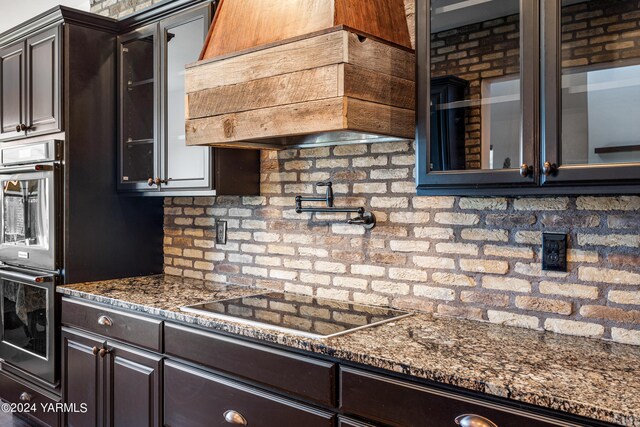 kitchen featuring black electric stovetop, premium range hood, glass insert cabinets, and dark brown cabinetry