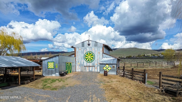 view of pole building with a rural view, gravel driveway, fence, and a mountain view