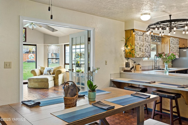 dining space featuring a textured ceiling, a textured wall, wood finished floors, and lofted ceiling