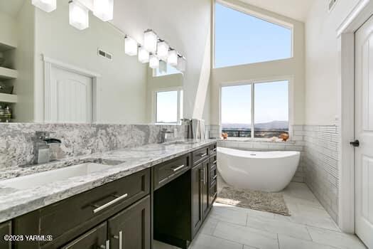 921 Tibbling Rd, Selah, WA 98942 - bathroom with a towering ceiling, healthy amount of natural light, double vanity, a freestanding bath, and a wainscoted wall