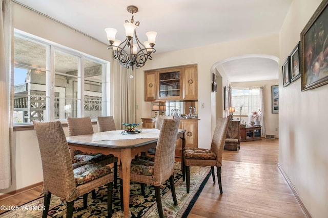 dining area with visible vents, arched walkways, light wood-type flooring, baseboards, and a chandelier