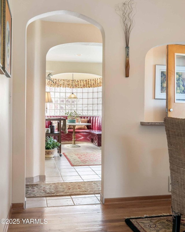 hallway featuring arched walkways, baseboards, and wood finished floors