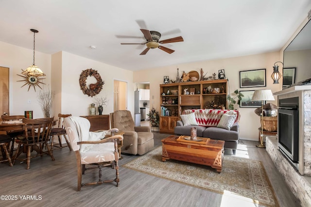 living area featuring a glass covered fireplace, ceiling fan, and wood finished floors