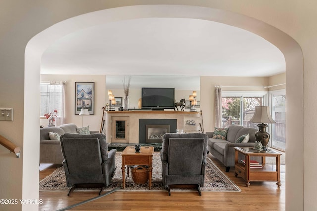 living area with a glass covered fireplace, arched walkways, and wood finished floors