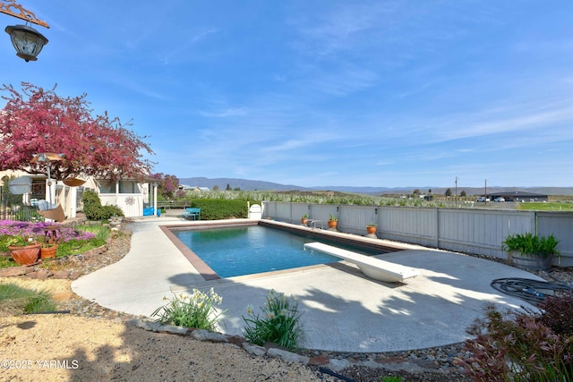 view of pool with a diving board, a fenced backyard, a fenced in pool, a mountain view, and a patio