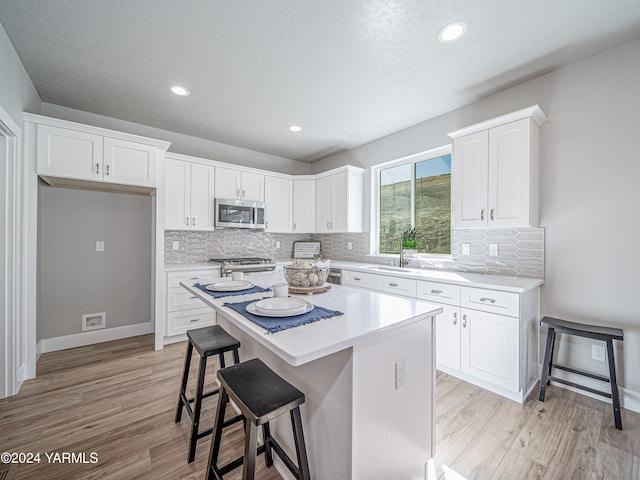 kitchen featuring a breakfast bar, a center island, light countertops, stainless steel microwave, and white cabinetry