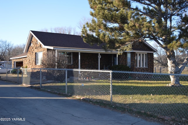 view of front facade with a fenced front yard, a shingled roof, stone siding, driveway, and a front lawn