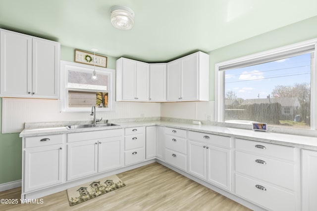 kitchen featuring light stone countertops, light wood-style flooring, a sink, and white cabinetry