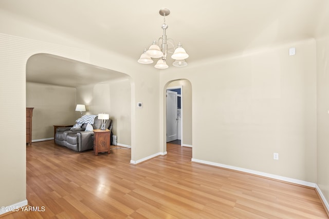 interior space featuring baseboards, arched walkways, an inviting chandelier, and light wood-type flooring