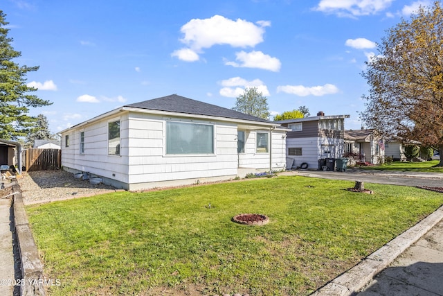 view of front of home with a shingled roof, a front lawn, and fence