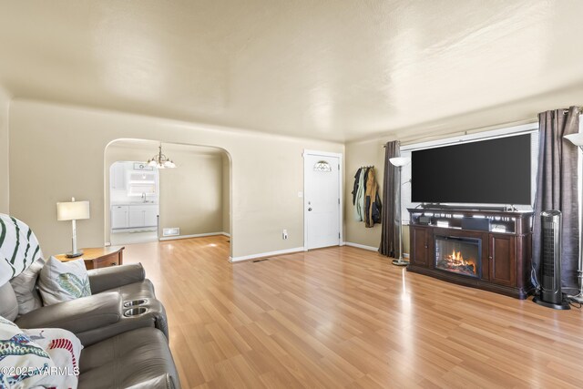 living room with arched walkways, a glass covered fireplace, light wood finished floors, and baseboards