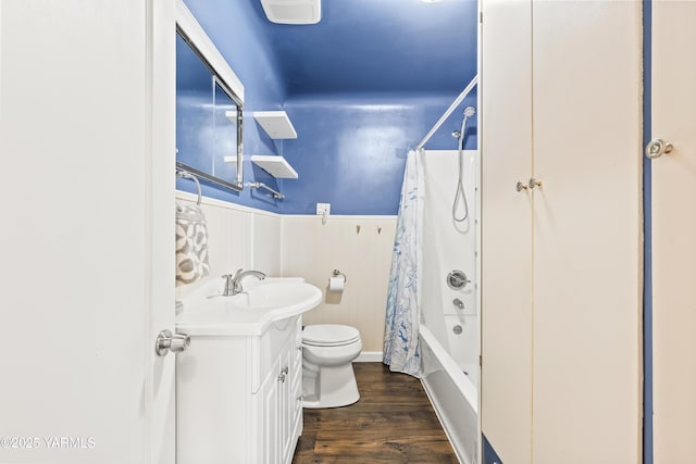 bathroom featuring wood finished floors, wainscoting, vanity, toilet, and shower / bath combo with shower curtain