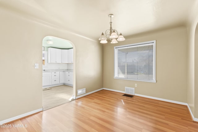 unfurnished dining area featuring arched walkways, a notable chandelier, visible vents, and light wood-style flooring