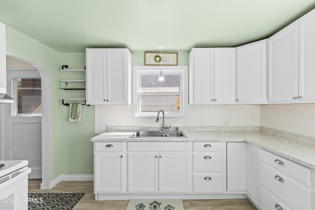kitchen with a sink, arched walkways, light wood-style flooring, white cabinets, and baseboards