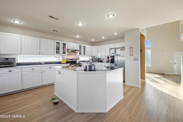 kitchen featuring dark countertops, white cabinetry, a kitchen island with sink, and glass insert cabinets