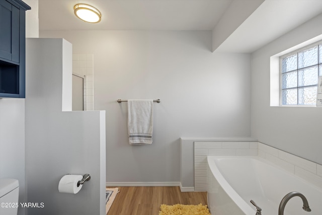 bathroom featuring baseboards, toilet, wood finished floors, a garden tub, and a shower stall