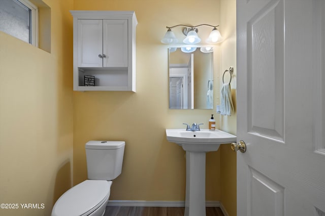 half bathroom featuring toilet, baseboards, and a sink