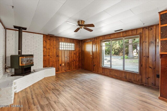 3803 Tieton Dr, Yakima, WA 98902 - unfurnished living room featuring ceiling fan, wood finished floors, a wood stove, wood walls, and baseboards