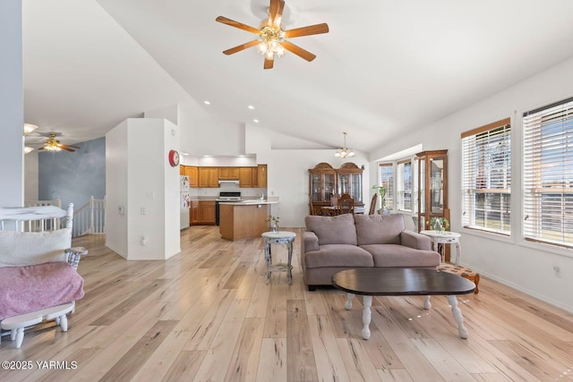 living room featuring baseboards, ceiling fan with notable chandelier, light wood-style flooring, and vaulted ceiling