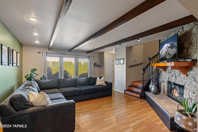 living area with a textured ceiling, light wood finished floors, beamed ceiling, and a fireplace