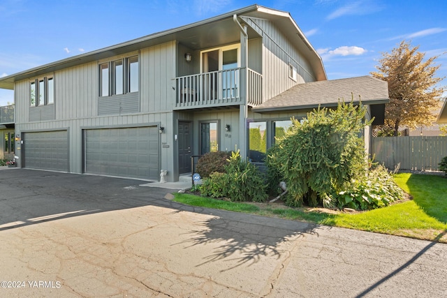 view of front of home with a balcony, driveway, an attached garage, and fence