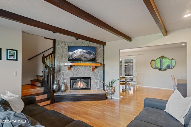 living room with baseboards, wood finished floors, stairs, a textured ceiling, and a stone fireplace