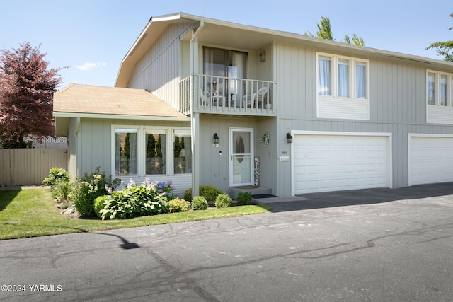 view of front of home featuring an attached garage, a balcony, fence, and aphalt driveway