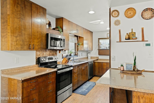 kitchen with light wood-style flooring, a sink, tasteful backsplash, appliances with stainless steel finishes, and light countertops