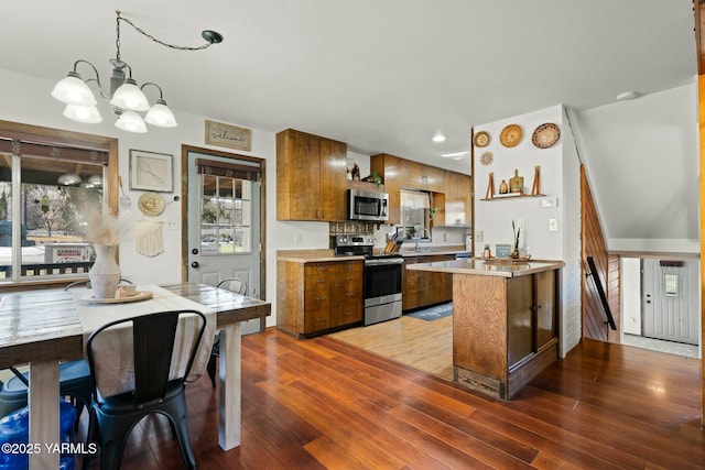 kitchen with light countertops, brown cabinets, a peninsula, wood finished floors, and stainless steel appliances