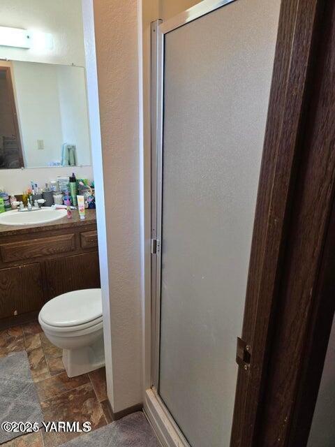 bathroom featuring toilet, a stall shower, stone finish floor, and vanity