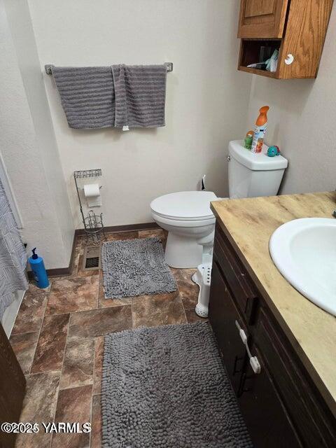 bathroom with stone finish flooring, vanity, toilet, and baseboards