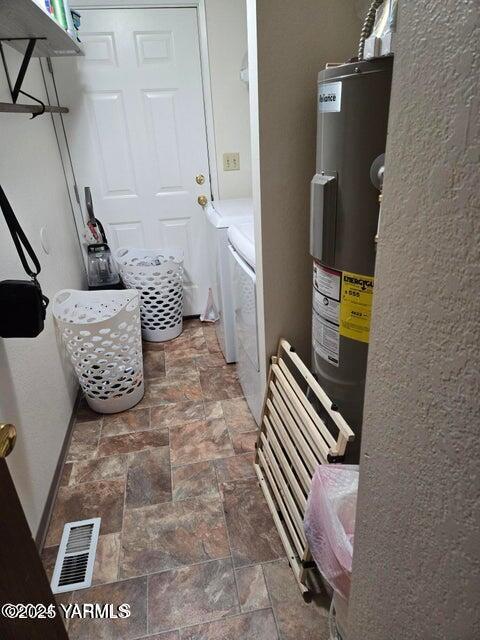 washroom featuring washing machine and dryer, laundry area, visible vents, water heater, and stone finish floor