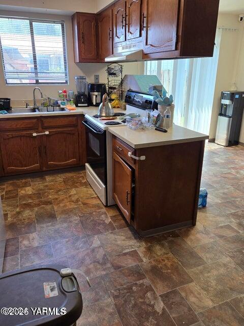 kitchen with electric range, stone finish floor, light countertops, and a sink