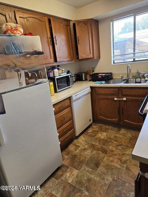 kitchen with brown cabinetry, white appliances, light countertops, and a sink