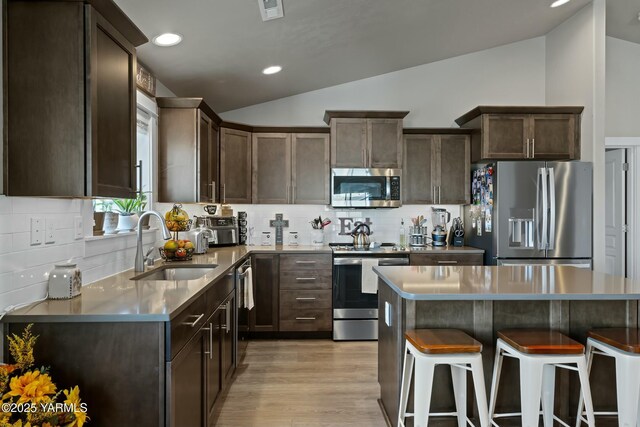 kitchen with a breakfast bar area, stainless steel appliances, a sink, vaulted ceiling, and a center island