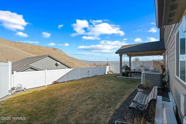 view of yard featuring a fenced backyard, a mountain view, central AC unit, and a patio