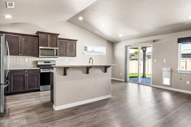 2201 S 62nd Ave, Yakima, WA 98903 - kitchen with appliances with stainless steel finishes, a breakfast bar area, vaulted ceiling, healthy amount of natural light, and dark brown cabinetry