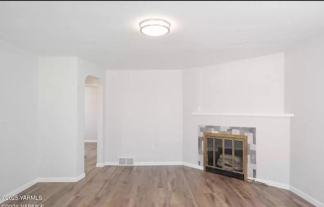 unfurnished living room featuring baseboards, visible vents, arched walkways, a tiled fireplace, and wood finished floors