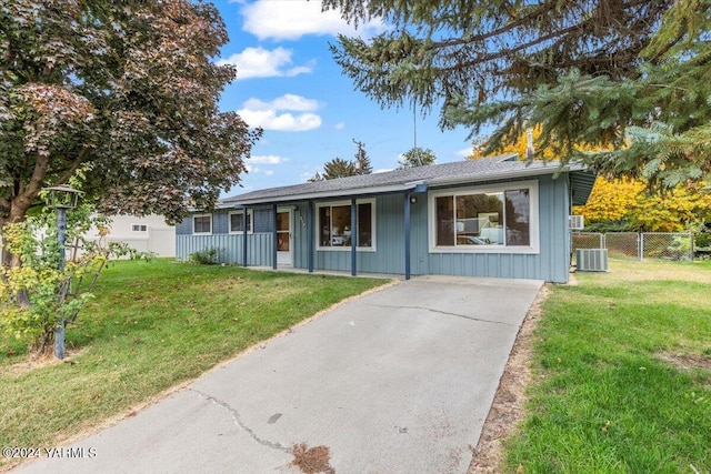 ranch-style house featuring board and batten siding, cooling unit, fence, and a front lawn