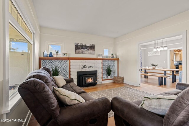 living area featuring a brick fireplace, light wood-style flooring, and baseboards