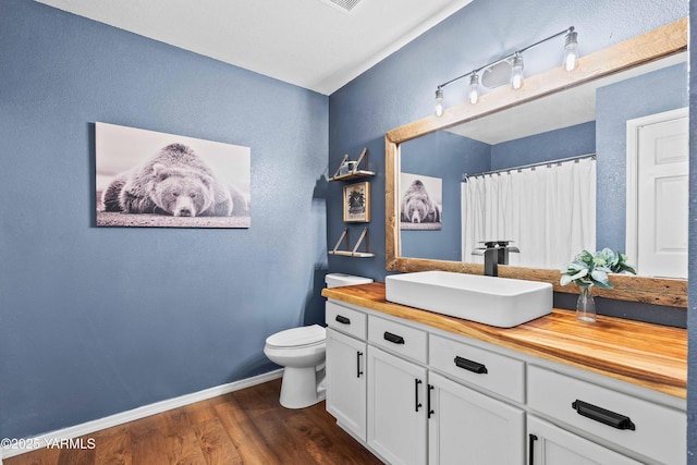 full bathroom with vanity, a textured wall, wood finished floors, toilet, and baseboards