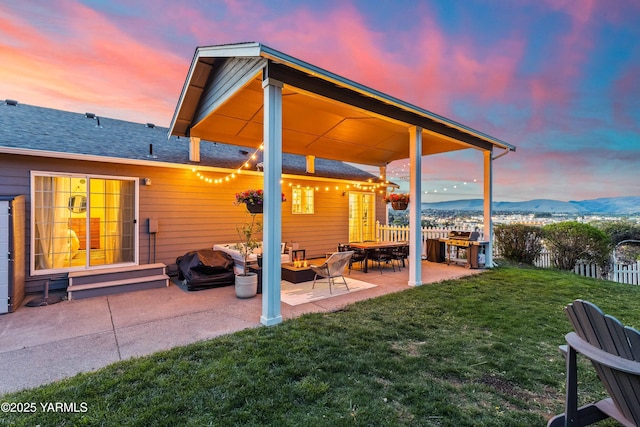 exterior space featuring roof with shingles, fence, a mountain view, a yard, and a patio