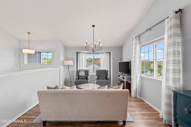 living area with baseboards, a notable chandelier, wood finished floors, and lofted ceiling