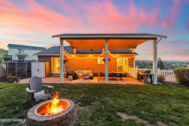 back of property at dusk with a patio, an outdoor living space with a fire pit, fence, and a yard