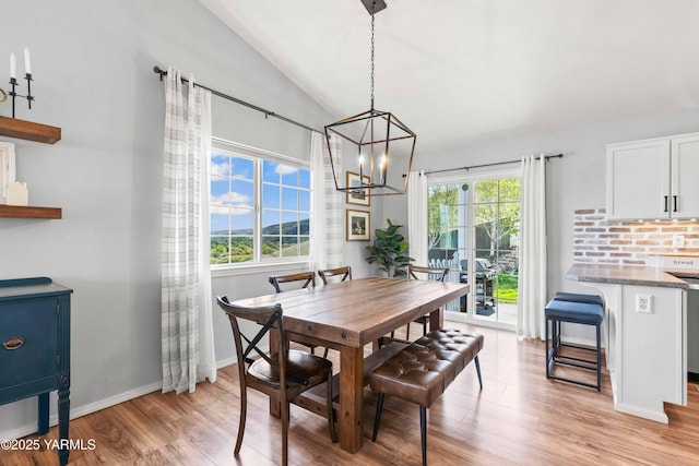 dining space featuring light wood-style floors, baseboards, a chandelier, and vaulted ceiling