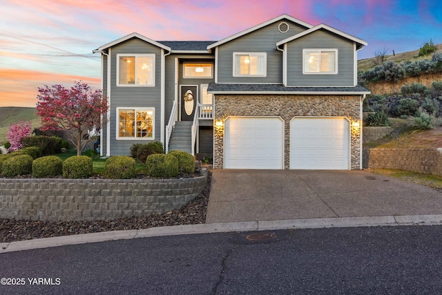 raised ranch with a garage, driveway, and stone siding