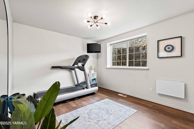 exercise room with baseboards, wood finished floors, and a chandelier